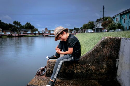 A boy sitting along the waterfront edge of Bayou St. John.