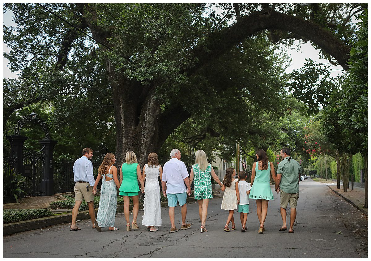 A large family wearing green and cream outfits walking hand and hand down a street.