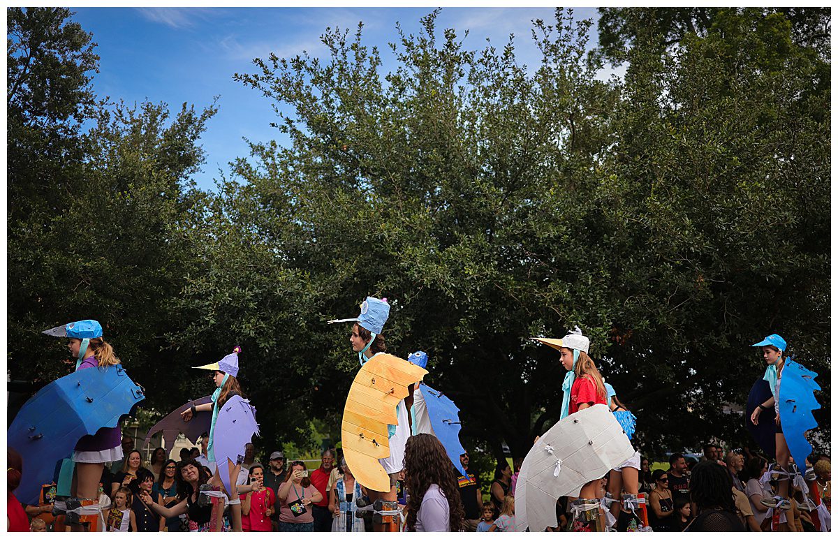 Several kids with bird costumes walking on stilts during a parade.