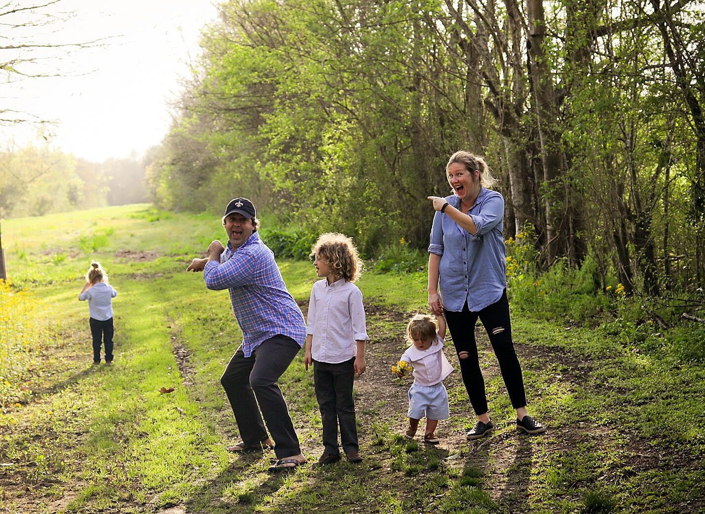 A family laughs with their middle child as he pouts and doesn't want to take family pictures.