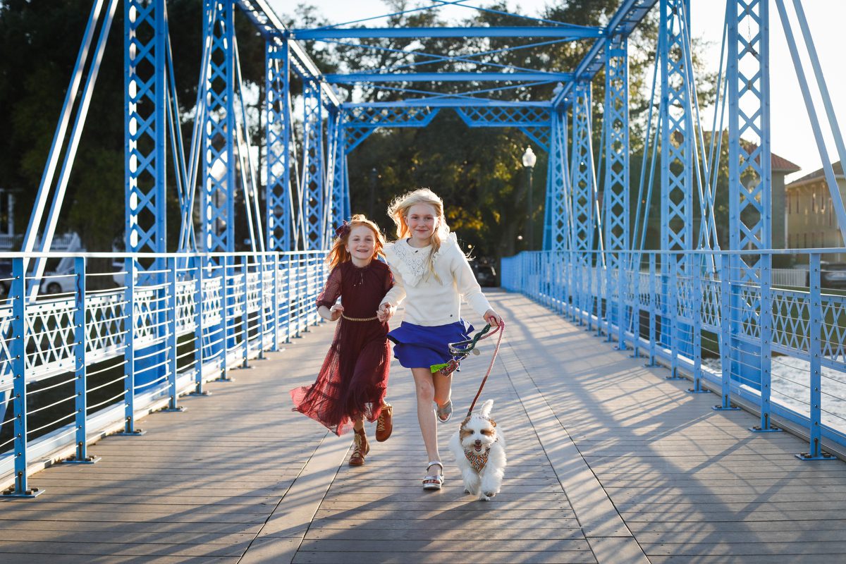 Two sisters and a dog running across a bridge for a story about how long does a family session take? A New Orleans photographer's honest answer.